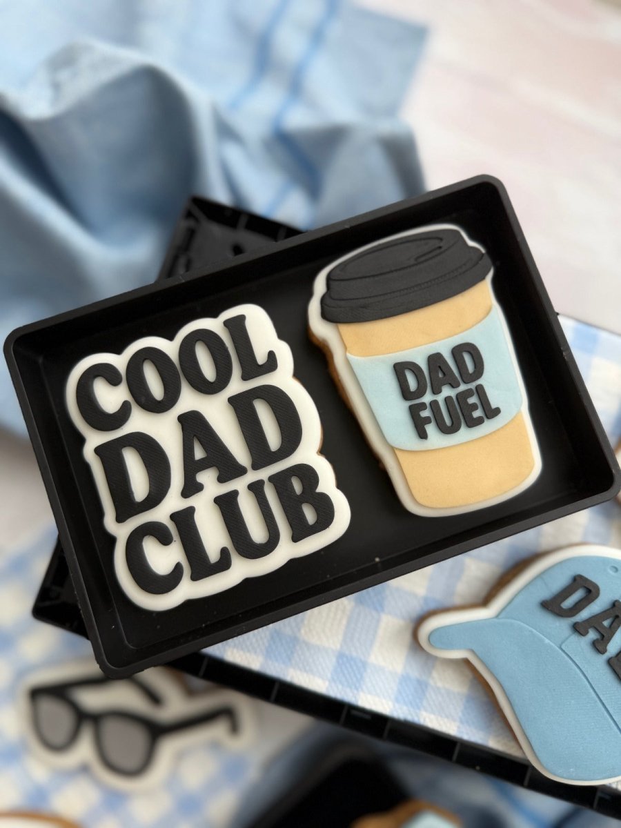 Koffiebeker koekje met Dad Fuel naast een Cool Dad Club koekje in een zwart doosje