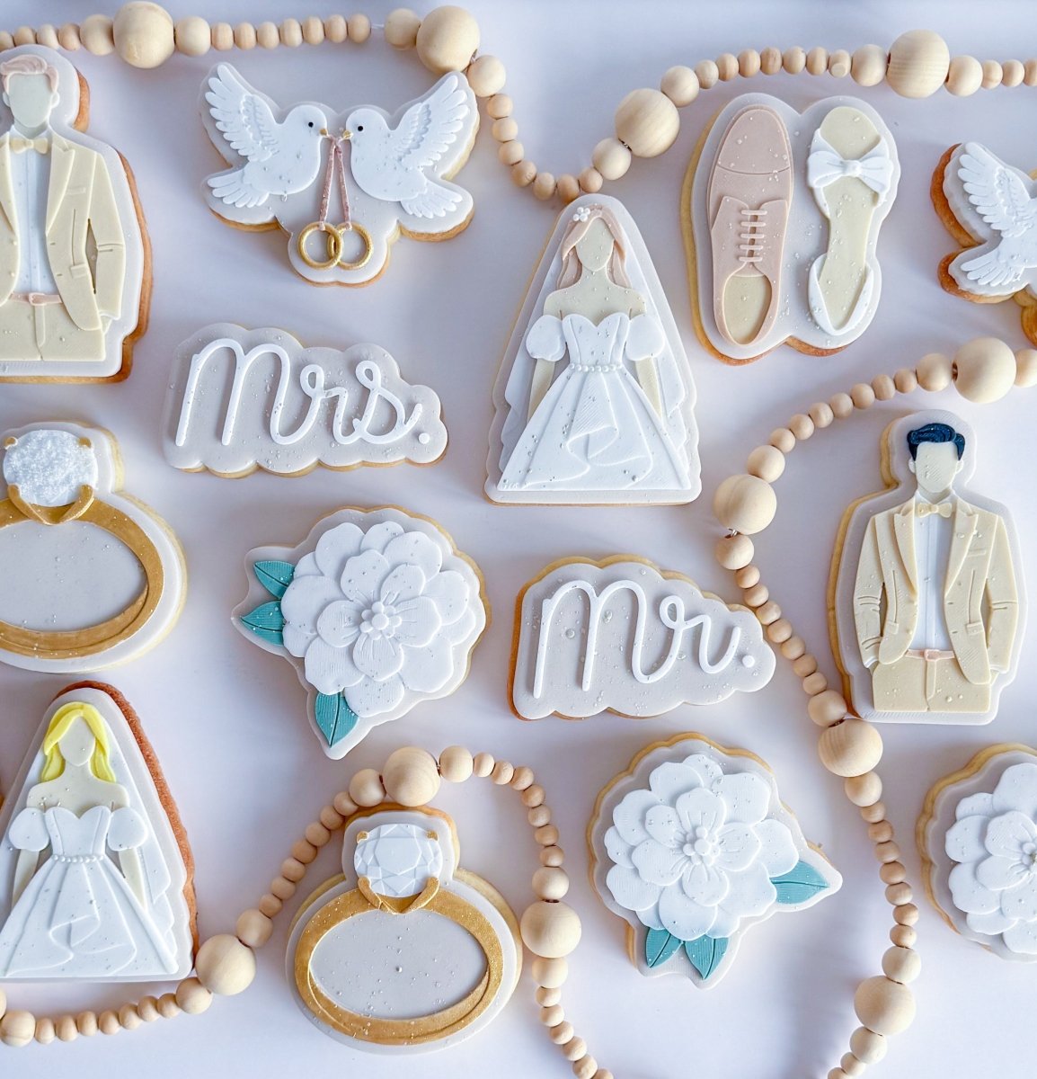 Overzicht van witte trouwkoekjes met Mr, Mrs, ringen en een bruidsjurk