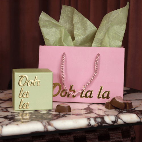 Cadeautas gevuld met groen vloeipapier op marmer, naast een groen doosje en hartvormige bonbons